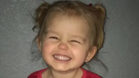 Natasha Broadley Louisana Dolan, with blonde hair in pigtails, smiling at the camera