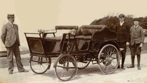 Public domain Three Victorian men next to a Stephens motor car. The photo is black and white