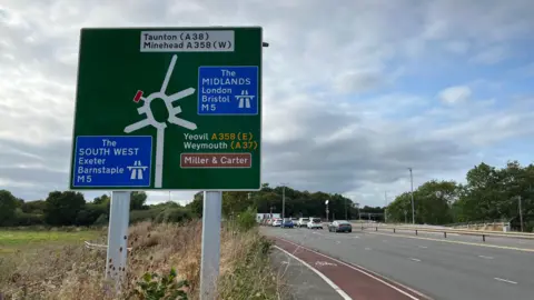 Roundabout sign showing the M5 and A358 roads with a roundabout in the background