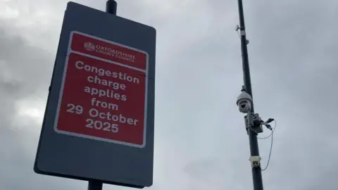 A red sign with a camera next to it. The sign reads congestion charge applies from 29 October 2025
