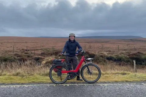 Harry Gray stands next to his bike at the side of the A57 Snake Pass