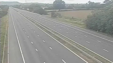 The M5 early on Saturday morning with no cars on it at all. There are fields and trees on either side of the motorway and the sky is grey. 