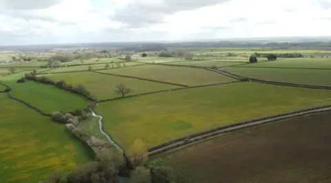 An aerial view of the farmland where the solar panels might be built. They are big, green fields with bush hedgerows.