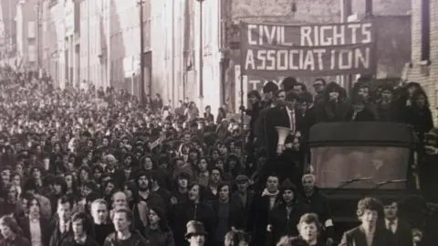 A black and white image of crowds gathered. People on the back of a truck are holding up a banner reading: "CIVIL RIGHTS ASSOCIATION".