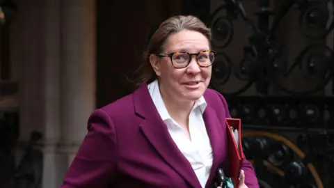 Minister without Portfolio, Anna Turley, arrives for a weekly government cabinet meeting at Downing Street on April 28, 2026 in London, England. She is wearing a dark pink suit and white shirt, with a red folder under her left arm.