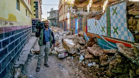 Bhasker Solanki An old picture shows Bhasker carrying his TV camera next to rubble from the  earthquake