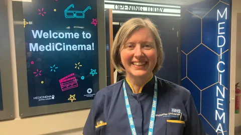 Photograph of Julia Birchall-Searle from the Manchester University NHS Foundation Trust. She is pictured in front of the MediCinema.