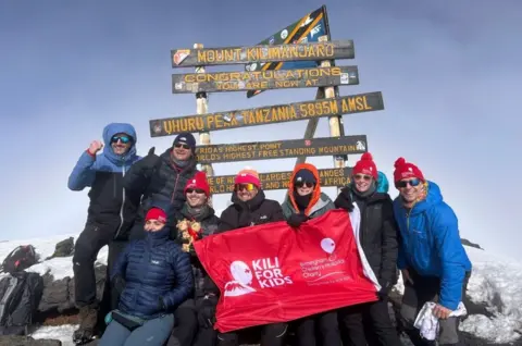 The Birmingham Women and Children Foundation trusts another group of eight people on the mountain, some of them holding a Kili for Kids banner. Behind them are the words: "Mount Kilimanjaro ... Congratulations that you are now on top of Uhuru"S