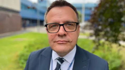 Det Ch Insp Adas is wearing a jacket and tie