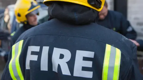 The back of a firefighter wearing uniform and a yellow helmet