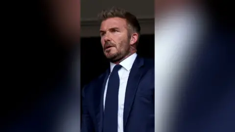 A man in a well tailored blue suit and tie, with a white shirt underneath.
