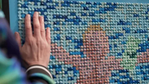 A replica of Nirvana's "nevermind" album cover made using a coloured mosaic of Braille. It depicts a more abstracted image of the album's cover - a baby floating underwater. 