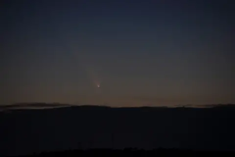 Meryl Goulbourne Una toma de larga distancia de un cielo nocturno oscuro desde la cima de una colina, con una luz brillante alejándose de la cámara.