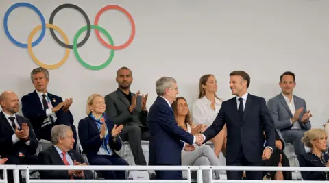   Martin Divíšek/EPA A smiling French President Emmanuel Macron (R) shakes hands with IOC president Thomas Bach as they take their seats in the Trocadero