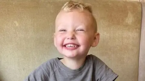 The late three-year-old Albie Speakman who has blond hair and a beaming smile wearing a grey t-shirt 