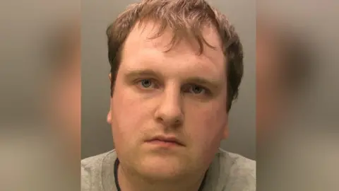 Cumbria Police Police custody image of Jonsen Lamb. He has brown hair and is wearing a grey jumper. He is looking into the camera.