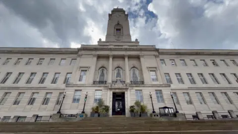BBC/James Vincent Barnsley's imposing Town Hall in a picture taken from a low angle at the bottom of the steps. Clouds are forming behind the white building.