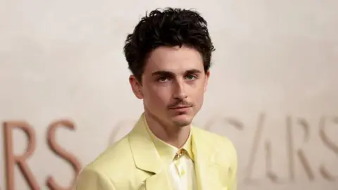 Getty Images Timothée Chalamet wearing a yellow suit and yellow shirt. He has short brown hair and holds a neutral expression