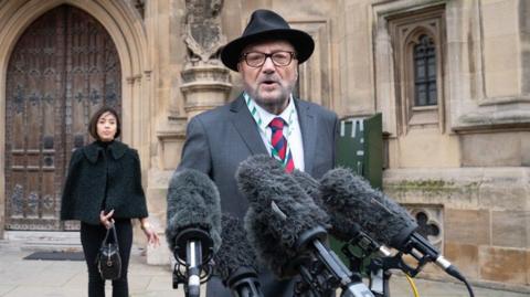 George Galloway speaks into a set of microphones 