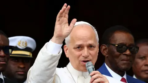 The Pope speaks into a microphone while raising his arm