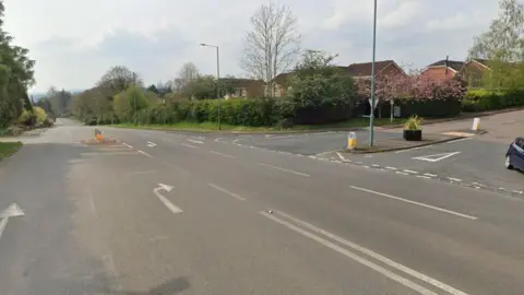 Google A screenshot from Google street view showing the junction where the accident occurred. It is a wide T junction with residential homes, hedges and trees neabry.