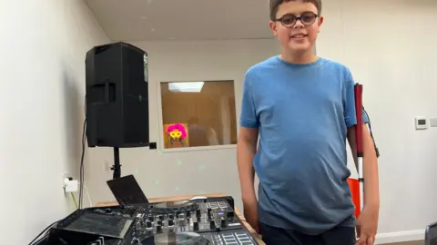 Jon Wright/BBC A boy in a blue t-shirt stands next to a DJ deck.