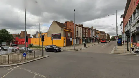 Google Traffic junction showing a street, traffic lights, a pedestrian island, and buildings either side, include a Vue cinema 