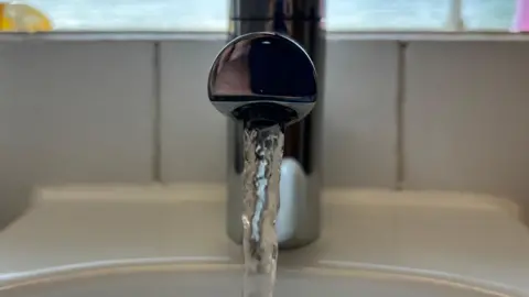 A close-up of a tap turned on with water spilling out of it.