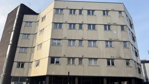 How the outside of the building currently looks, a beige and brown colour of different flats