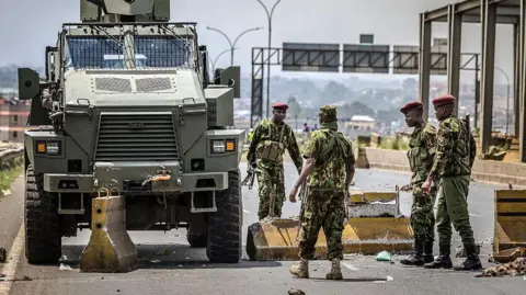 AFP via Getty Images four police officers standing next to an armoured vehicle on a road that has barricades