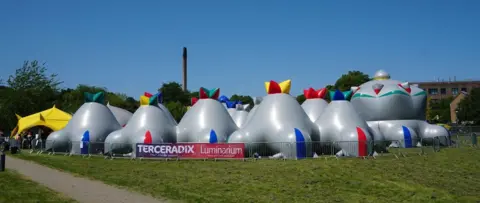 Architects of Air An outside view of the Luminarium Terceredix. The picture shows about a dozen grey dome-like structures.