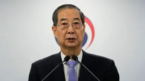 Close-up of Han Duck-soo speaking at a press conference with two microphones in front of his face.