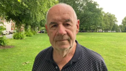 Man with a black polo shirt on and short/bald hair.