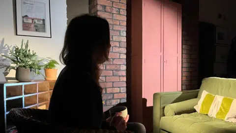 Woman sitting on a chair in a lounge. She is sitting in the dark and you cannot see her face to protect her identity.