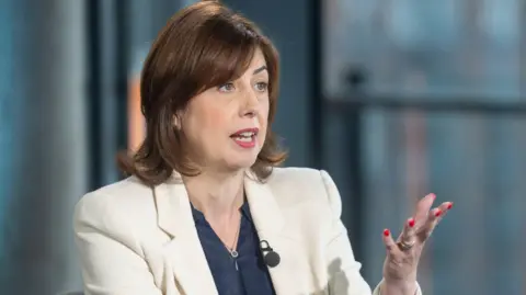 PA Media Lucy Powell, new deputy Labour leader, seated indoors on the BBC One programme Sunday with Laura Kuenssberg. She is wearing a cream blazer over a dark top, with a lapel microphone attached. One hand is raised in a gesturing motion, and the background shows large glass windows.