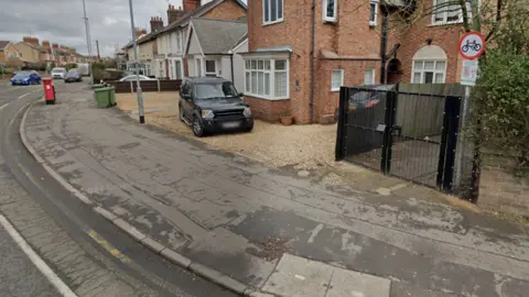 Google A black metal gate at the entrance of an alleyway with a red and white circular cycle sign above it.