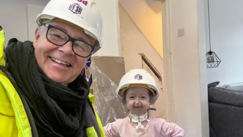 Supplied A selfie of Ian Hodgkinson in a high-vis jacket and white hard hat with Isla, also wearing a hard hat and smiling.