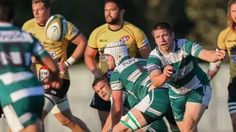 Martin Gray A rugby ball is thrown to a player in a white and green hooped top by another player with other players looking on.