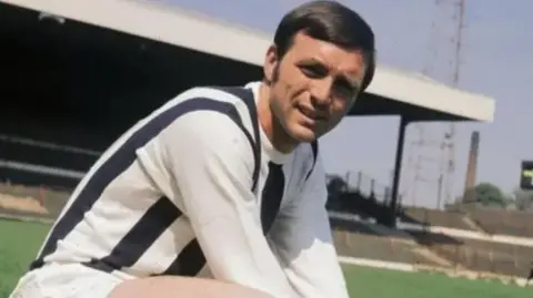 Getty Images Picture of Jeff Astle on the pitch of the Hawthornes Stadium during his playing days at West Bromwich Albion. He is wearing a dark blue and white stripped kit with white shorts. 