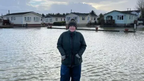 Sarah Dyke MP Sarah Dyke in waterproof coat and trousers standing in floodwaters in a caravan park