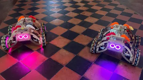 Two small robots with glowing headlight eyes on the floor of St George's Church in Gravesend