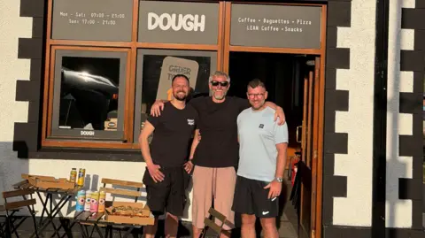 Jamie Watkins Three men stood outside a pizza shop 