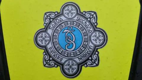 An Garda Síochána emblem on a yellow high viz jacket. 