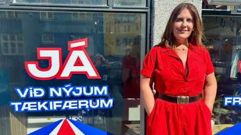 A woman in a red dress stands next to a window where the message is a distinct JA for yes in the referendum
