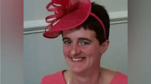 Family handout A woman wearing a pink fascinator and pink outfit smiles at the camera.