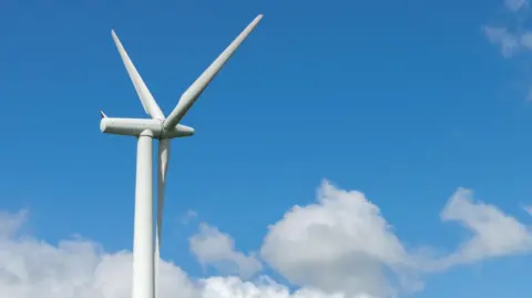 Getty Images A generic image of a wind turbine. It has three blades and is white in colour. The turbine is pictured against a blue sky with fluffy white clouds.