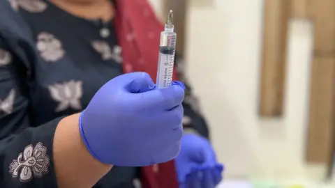 A woman's hand in a blue surgical glove holding a syringe