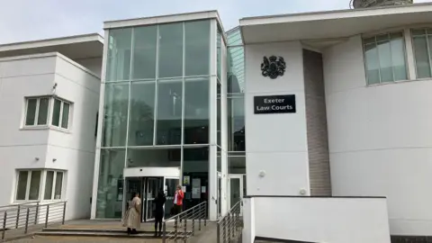 A white, modern court building with a glass entrance. A sign says "Exeter Law Courts".