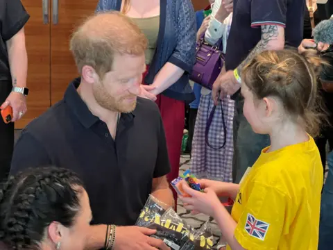 Prince Harry speaking to a young girl in a yellow shirt at a party for bereaved children of military personnel
