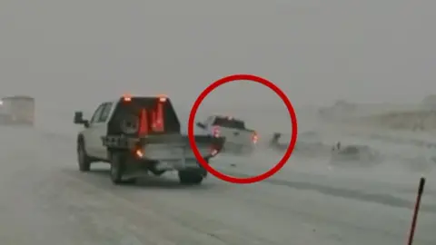 A vehicle circled in red nearly collides with a person on the side of a white snow-covered road as another service truck drives nearby in the foreground.